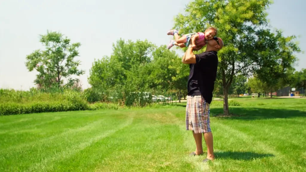 Man lifting small child in the air standing in a park