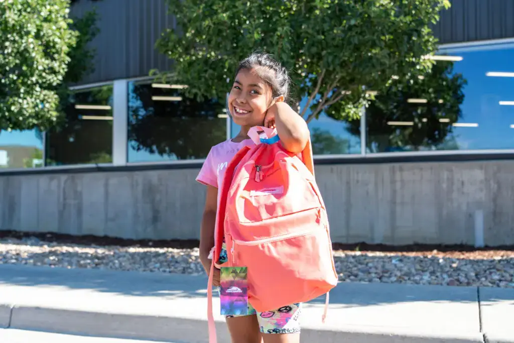 A young girl smiling and showing off her new pink backpack.