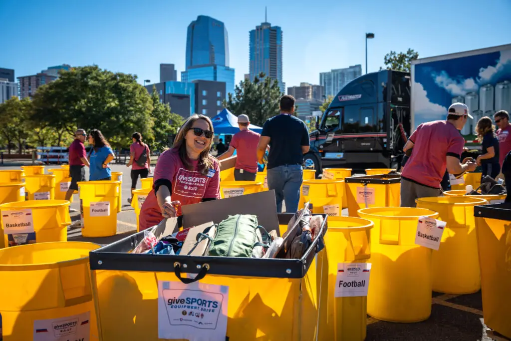 A volunteer smiling with a full donation bin during the giveSPORTS equipment drive.