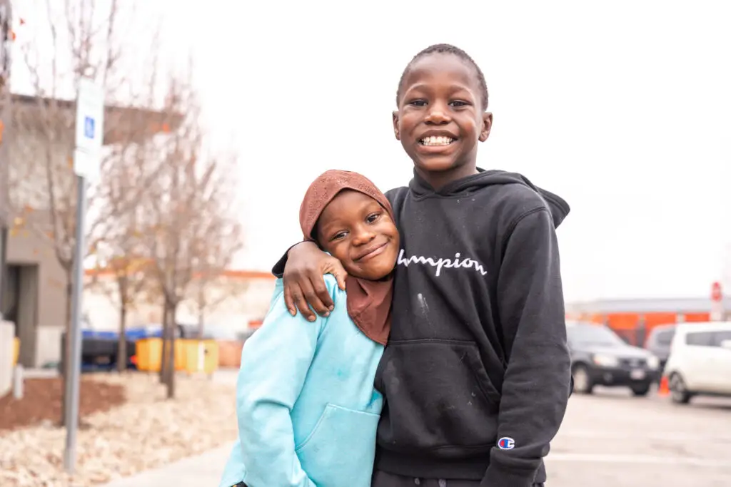 Two siblings, a brother and sister, hugging and smiling at A Precious Child facility.