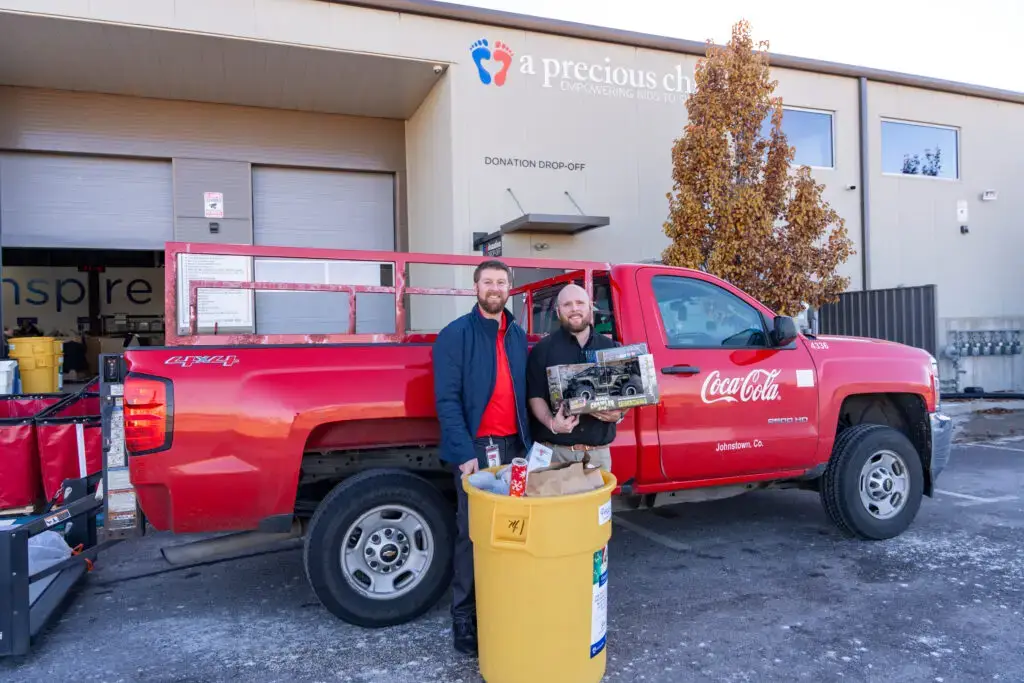 Two sponsors smiling and showing the presents they are donating to A Precious Child.