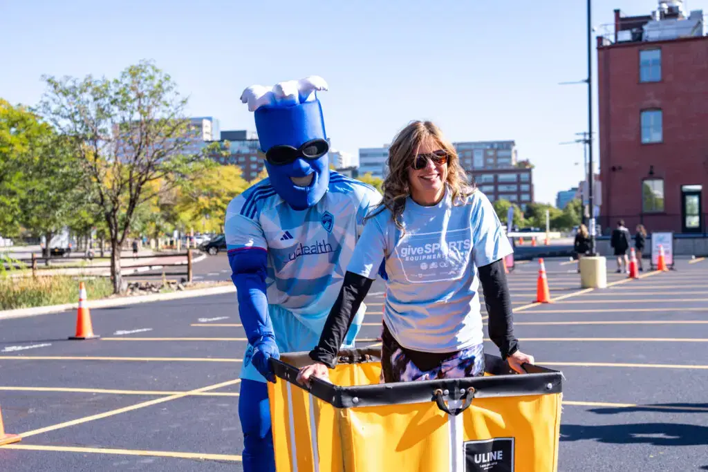 A volunteer smiling with RapidMan, the Colorado Rapids mascot.